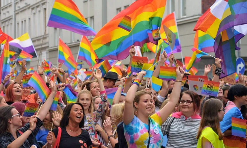 Group of people protesting as part of a pride parade. Everyone is waving various pride flags, all of different sizes.