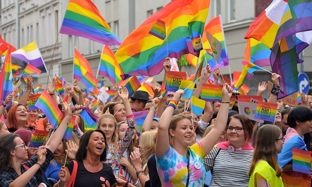 Group of people protesting as part of a pride parade. Everyone is waving various pride flags, all of different sizes.