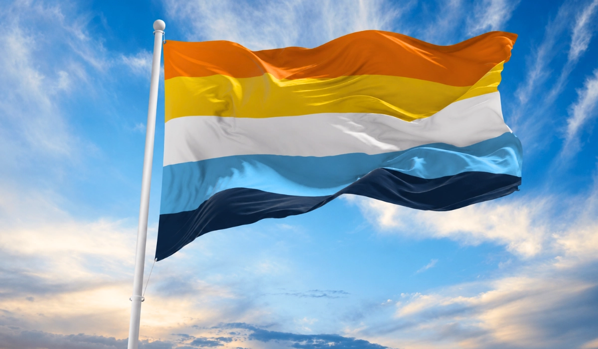 Sunny sky behind the sunset aroace flag waving in the wind attached to a white flag pole.