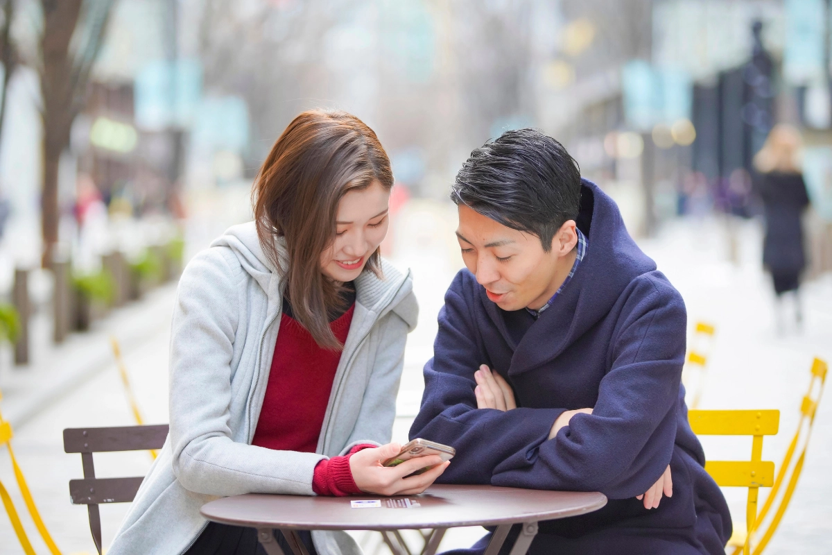 What Is It Like to Be Bisexual in Japan? 16 Two people sitting at an outdoor café table, looking at a smartphone together.