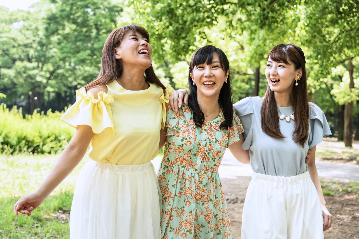 What Is It Like to Be Bisexual in Japan? 14 Three women walk together through a sunny park, smiling and laughing with their arms around one another.