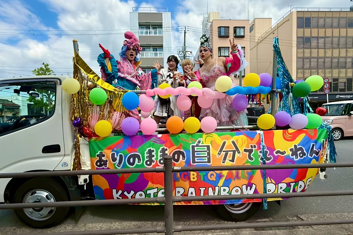 Drag queens stood on the back of a float surrounded by streamers and balloons at Kyoto Rainbow Pride
