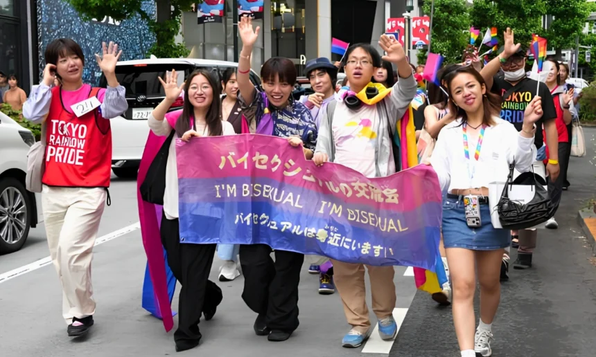 Participants in the Tokyo Rainbow Pride parade march while holding a bisexual pride banner reading “I’M BISEXUAL,” with bisexual and rainbow flags visible around them.