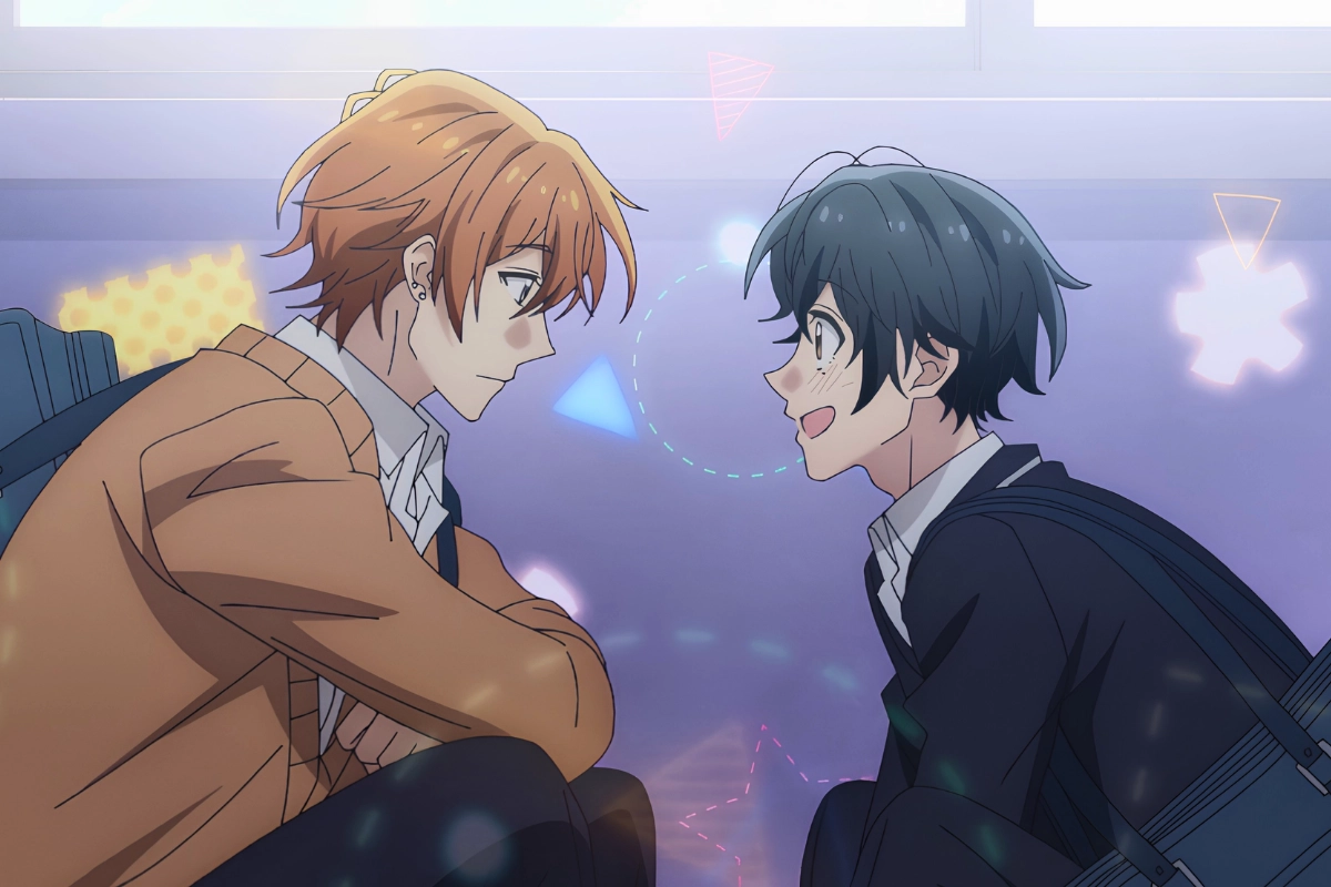 Two male students sit facing each other in school uniforms, smiling and talking in a softly lit setting.