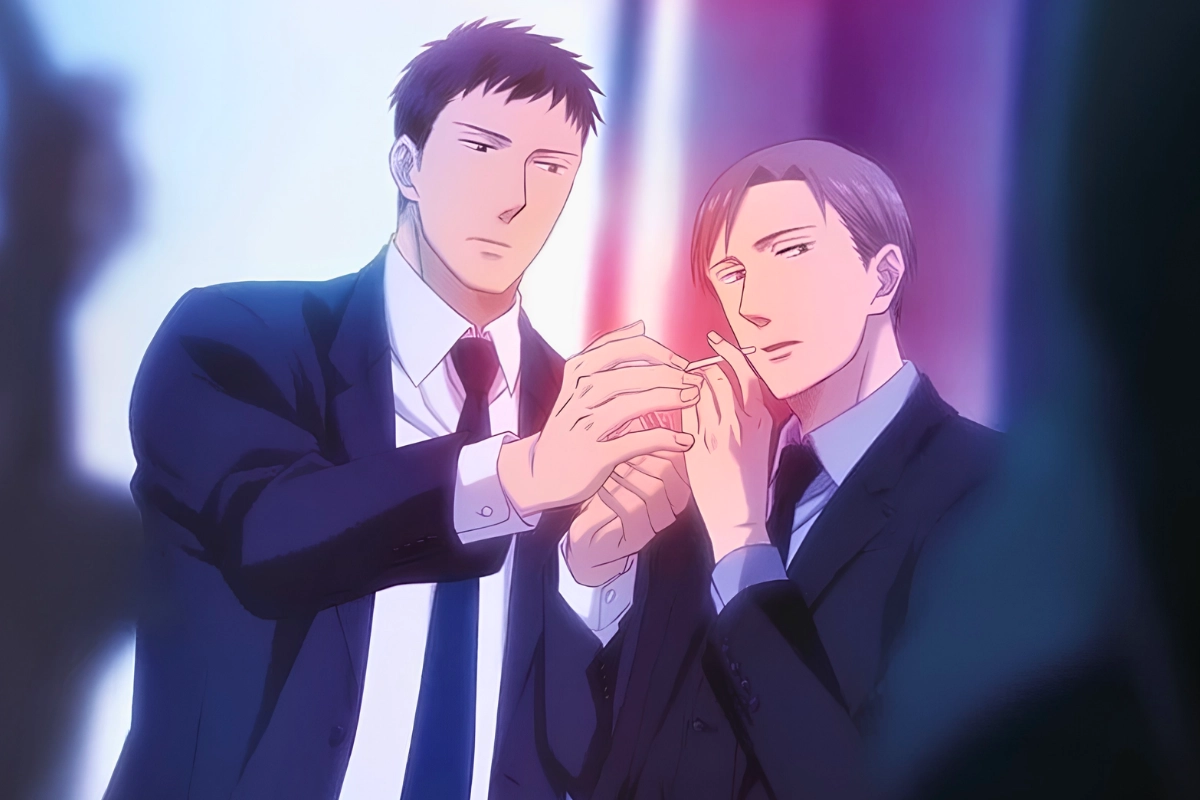 Two men in dark suits stand closely together while gently holding each other’s hands in a softly lit scene.
