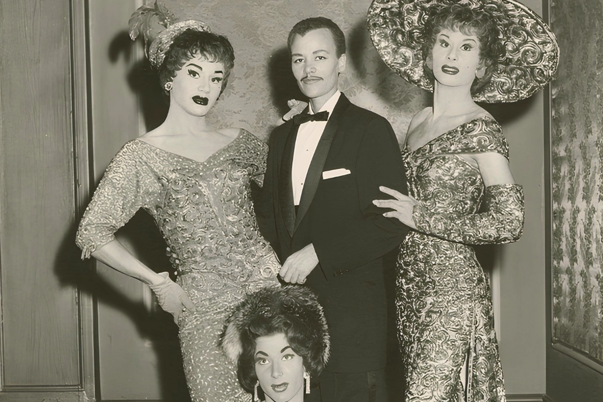 Masc Lesbian Meaning: How Masc Differs From Butch 13 Black-and-white vintage photograph of four performers posing together, with one wearing a tuxedo and the others dressed in elaborate gowns, hats, and stage makeup.
