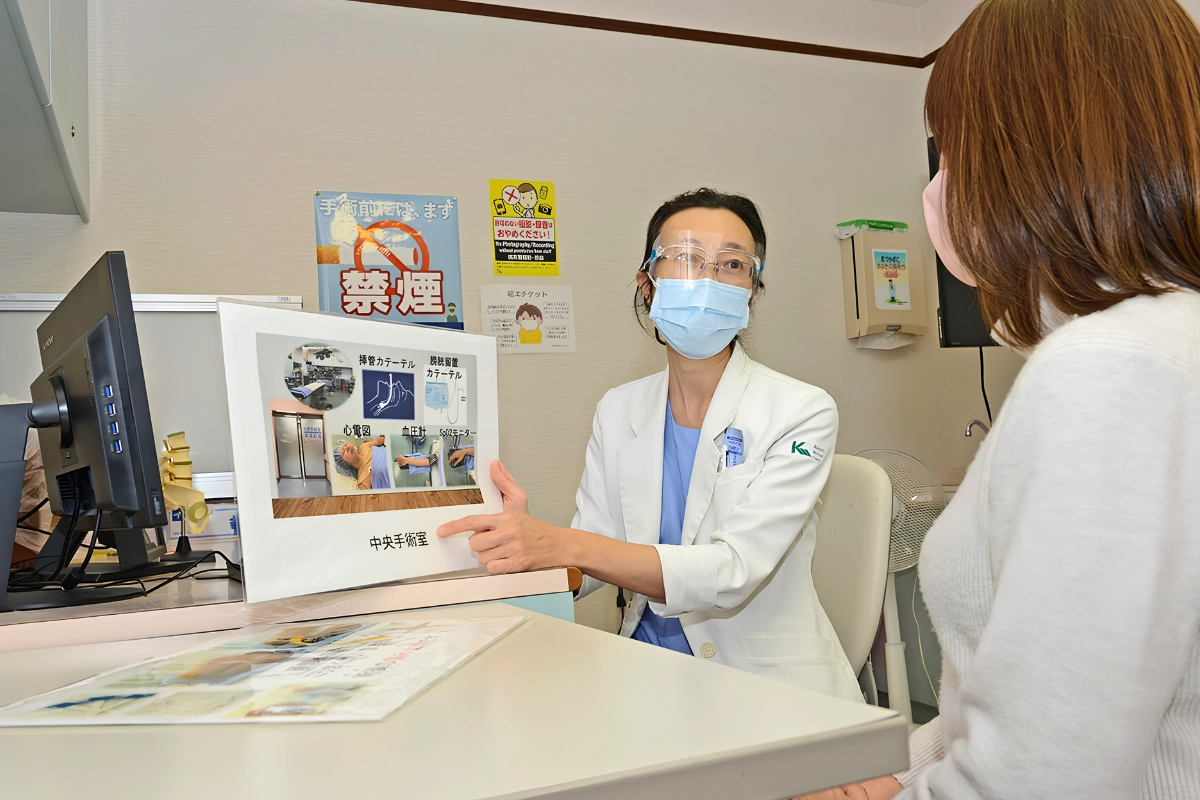 Getting Gender-Affirming Surgery in Japan: Providers, Costs and Preparation 12 Doctor wearing a mask and face shield explains operating-room equipment to a seated patient during a preoperative hospital consultation.