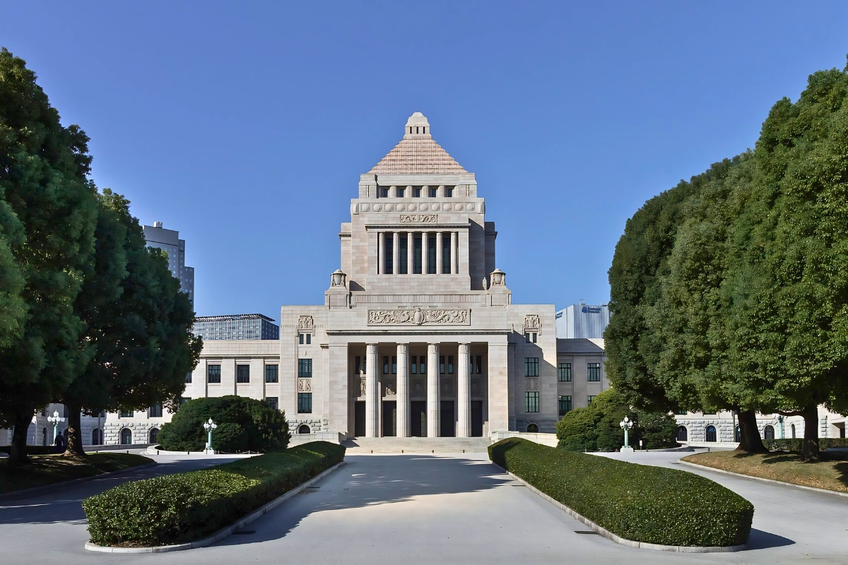 Exterior of Japan’s National Diet Building in Tokyo, framed by trees and hedges under a clear blue sky.