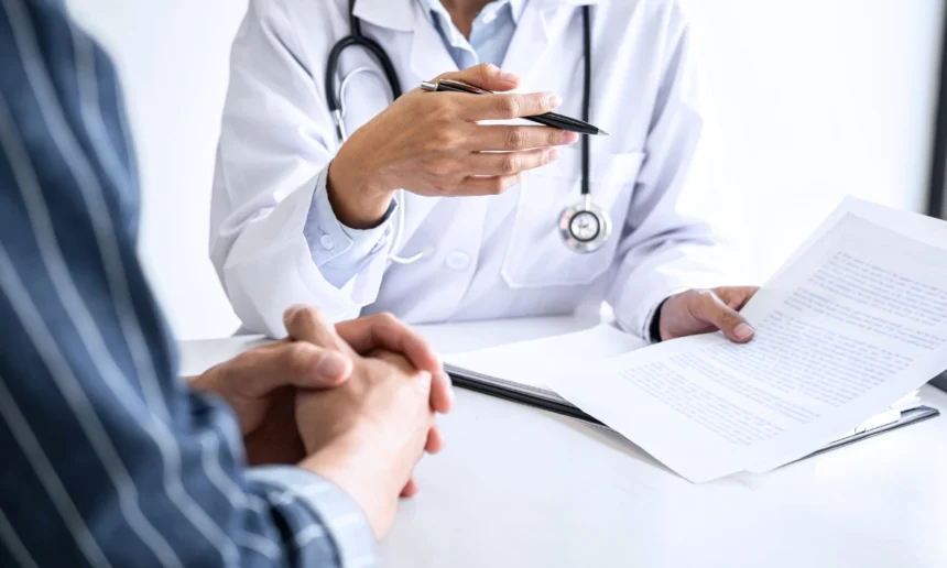 Doctor with a stethoscope discusses medical paperwork with a seated patient during a consultation.