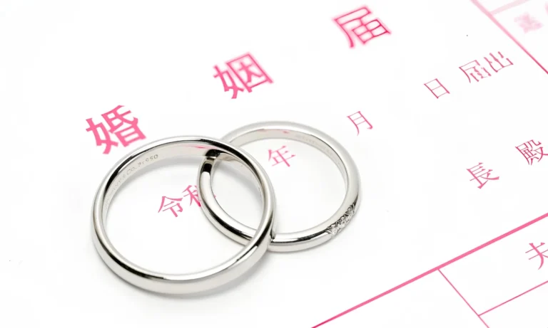 Two silver wedding rings resting on a blank Japanese marriage registration form, or kon’in todoke, with pink Japanese text visible in the background.
