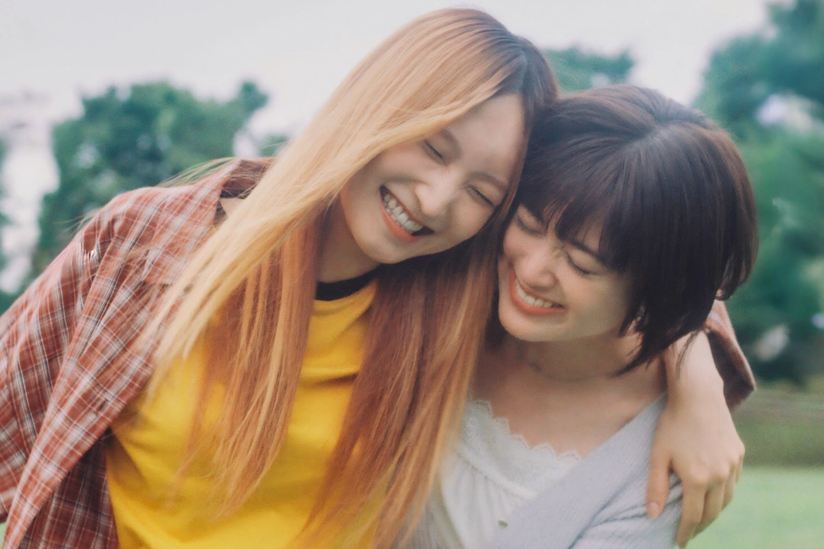 10 Best Japanese Lesbian Movies & Series to Watch 24 Two women smile with their eyes closed as they lean their heads together outdoors, one with long light hair and the other with a short dark bob.
