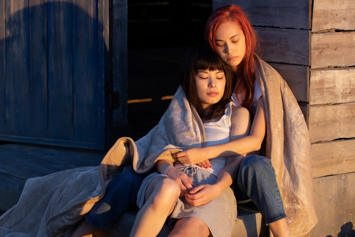 10 Best Japanese Lesbian Movies & Series to Watch 17 Two women sit closely together wrapped in a blanket, one resting against the other as they embrace in warm evening light.