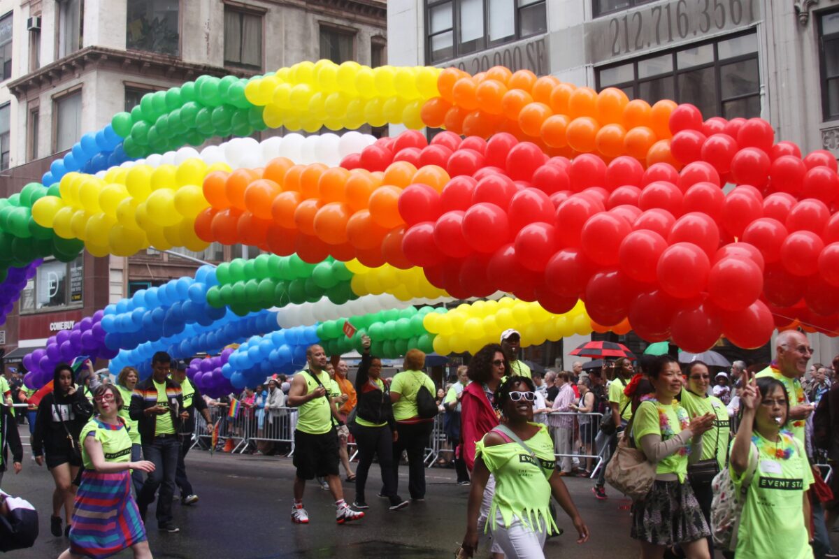 Marchers, flanked by volunteers, walk through New York underneath a float of rainbow-colored balloons