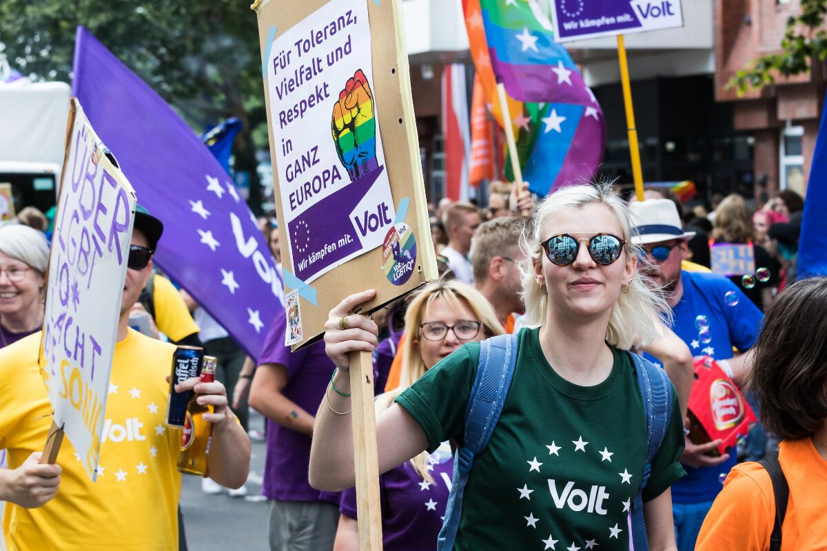 Marchers walk through a street in Cologne during Pride. In the center, one marcher holds a sign reading “For tolerance, diversity and respect throughout Europe”