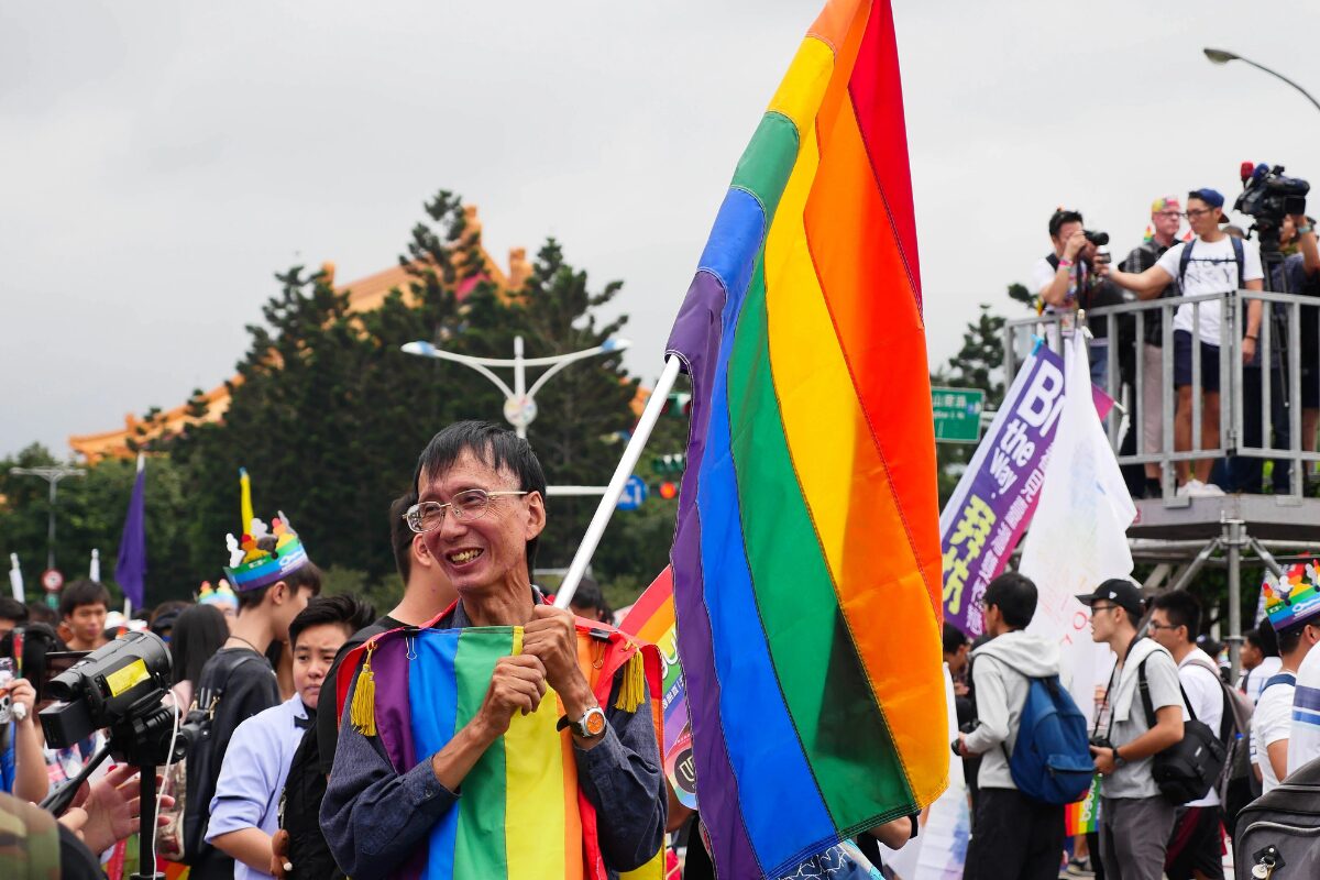 Marchers at Taiwan LGBTQ+ Pride. A man front and center wears a rainbow-colored poncho, and is holding a rainbow-colored flag
