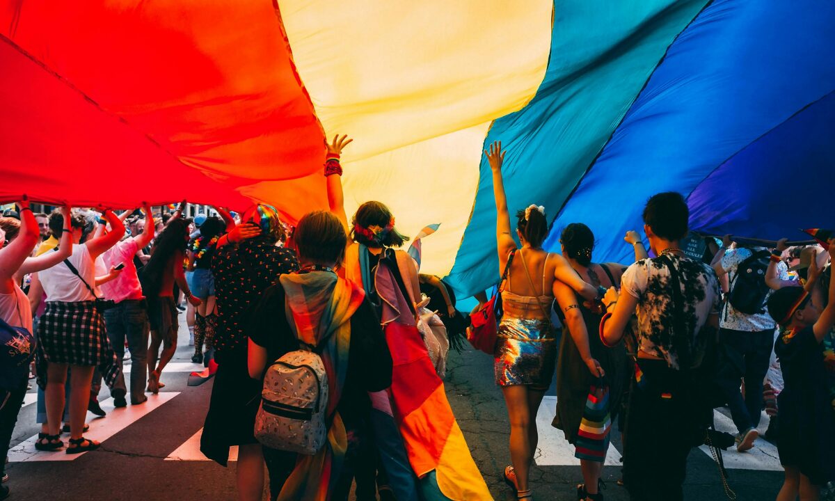 Marchers walk beneath a giant rainbow flag at a Pride Parade