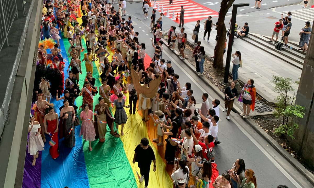 Marchers at the Bangkok Pride Festival walk down the street on top of a giant rainbow flag