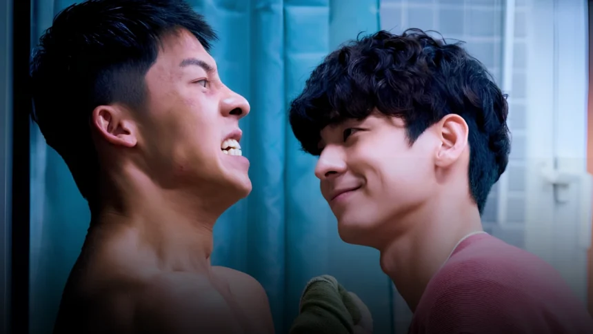 Two young men face each other closely, one smiling and the other smirking, against a blue background.