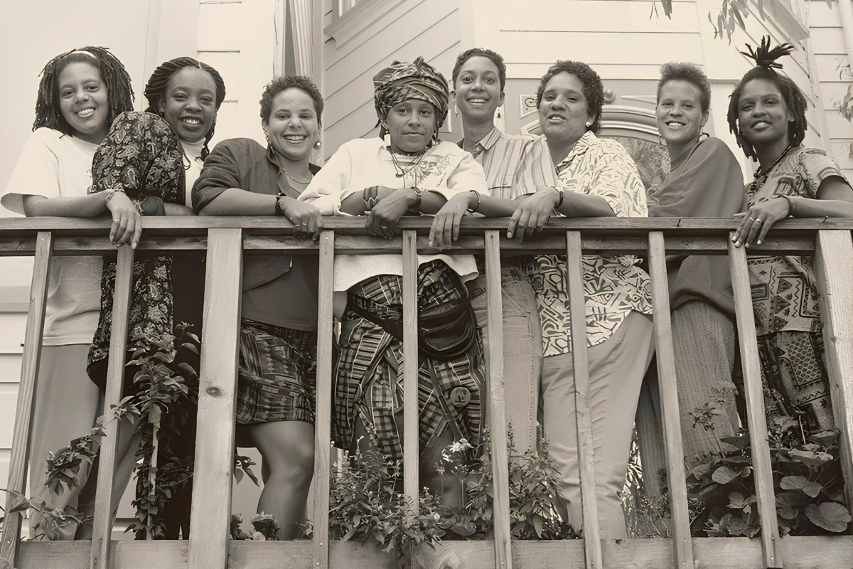 What Is a Stem Lesbian? Meaning, Origin, and Cultural Context 12 Black-and-white group portrait of eight Black women standing closely together on a wooden porch, smiling and leaning against the railing.