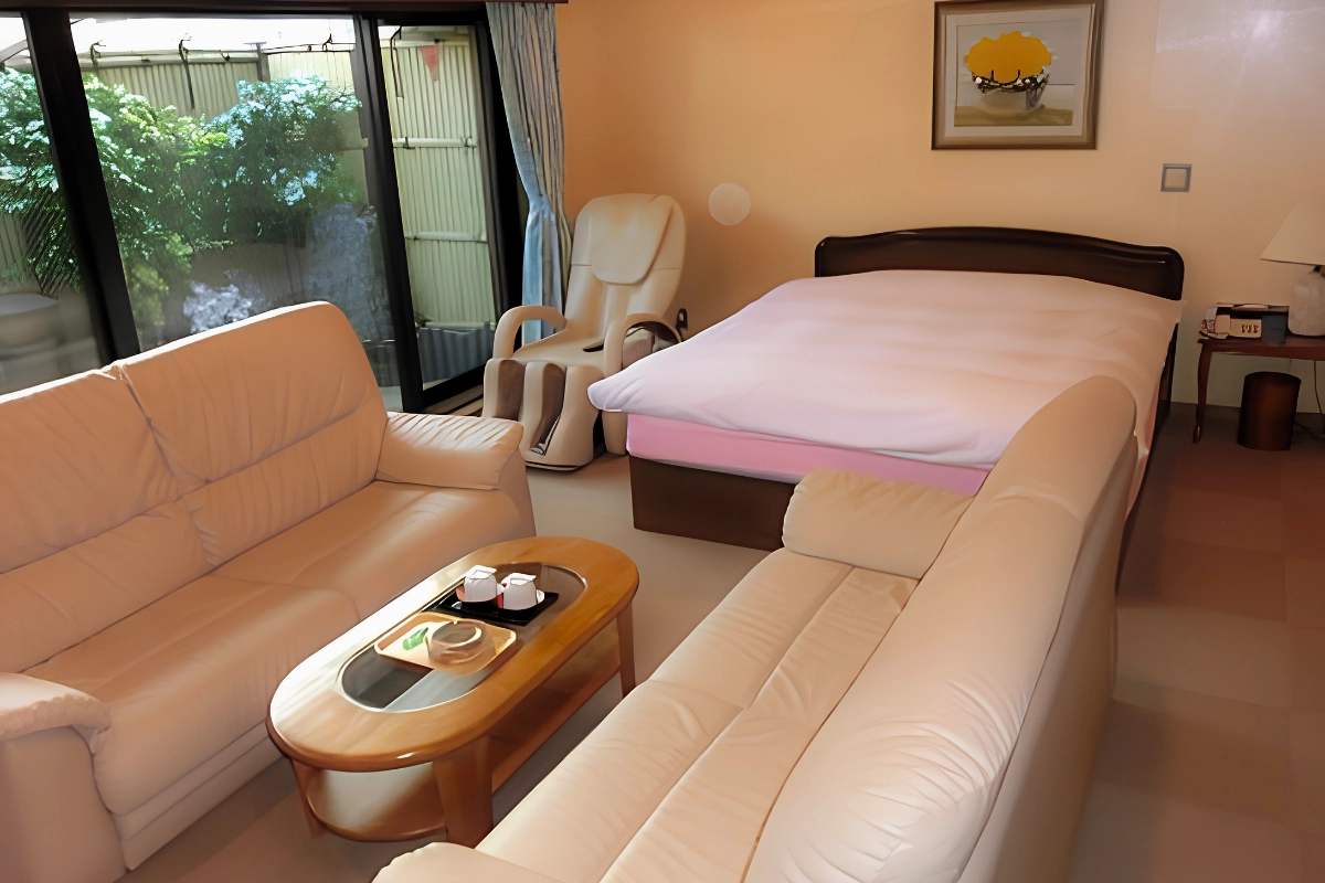 Private room at 24 Kaikan Shinjuku with a large bed, leather sofas, massage chair, and coffee table.
