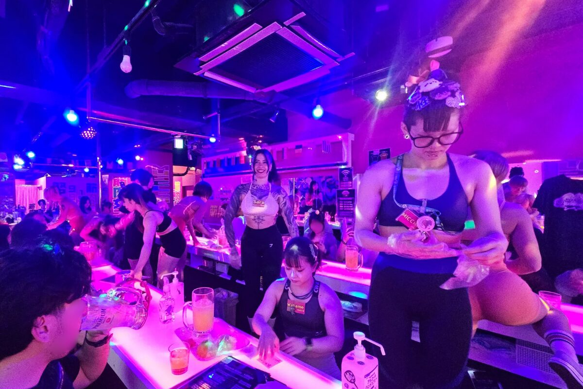 Muscle Girls Bar Tokyo: Prices, Reservations & What to Expect 12 Muscle Girls Bar staff serve their customers at the bar, which is light by purple neon light
