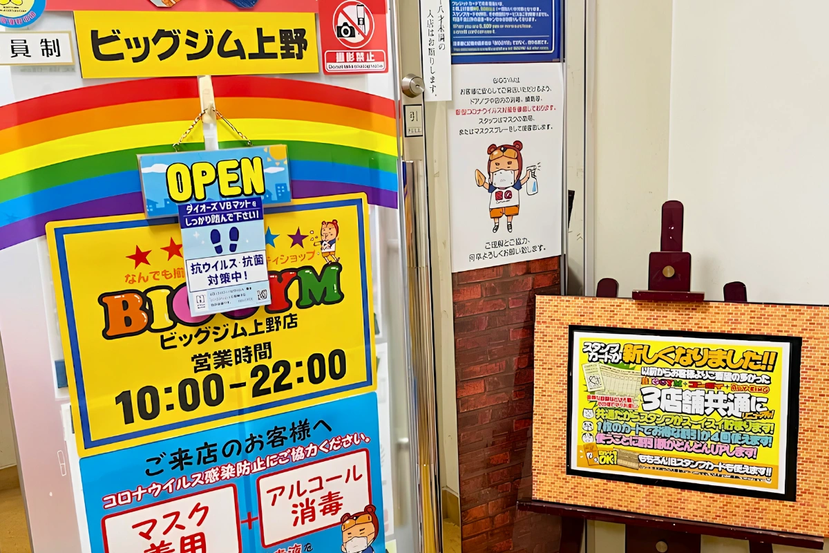 Entrance to BIGGYM Ueno covered with rainbow graphics and colorful Japanese signs, including opening hours and visitor notices.