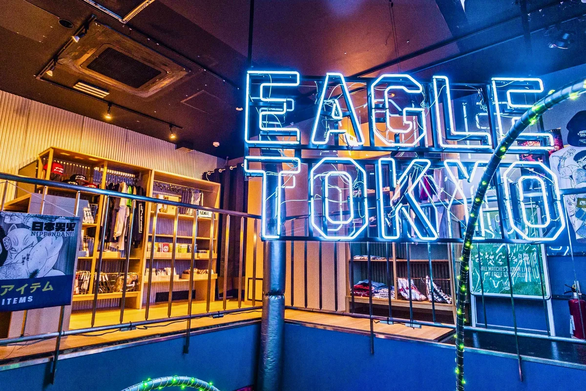 Interior of Eagle Tokyo, featuring a large blue neon “EAGLE TOKYO” sign above shelves and displays of clothing, accessories, and merchandise.