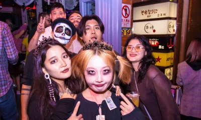 Group of costumed partygoers pose together outside nightlife venues during a Halloween event in Japan.
