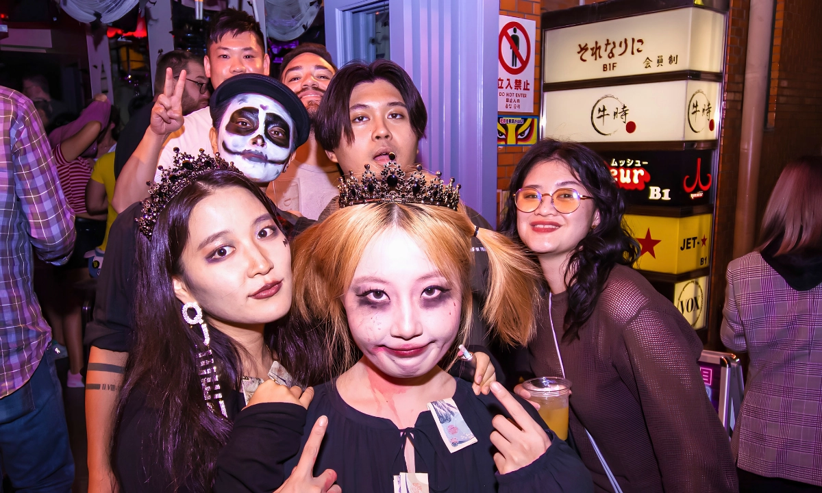 Group of costumed partygoers pose together outside nightlife venues during a Halloween event in Japan.