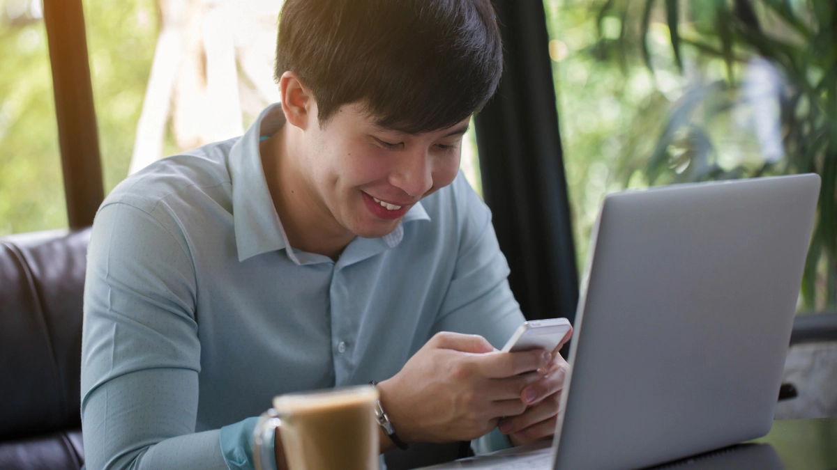 Hooking Up in Japan: A Guide for Gay and Bisexual Men 14 Young man smiling while using his smartphone beside a laptop.