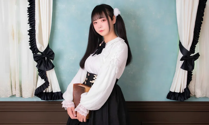 Person wearing a black-and-white kawaii fashion outfit with lace-trimmed sleeves, twin tails and fluffy hair accessories, posing indoors while holding a book.