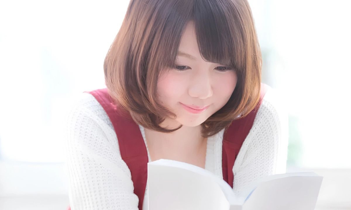 Young Japanese woman is led on their front smiling and reading a manga.