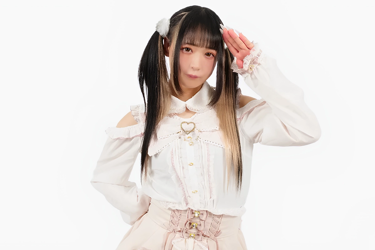 Person in a pale pink-and-white frilled outfit with twin tails and fluffy hair accessories posing against a plain white background.