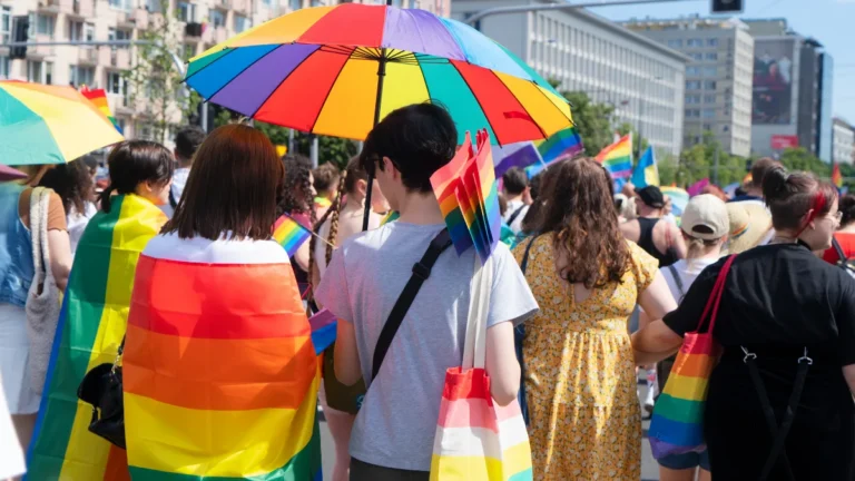 Participants celebrating at a Pride parade festival with rainbow flags and umbrellas, representing the global LGBTQ+ community.