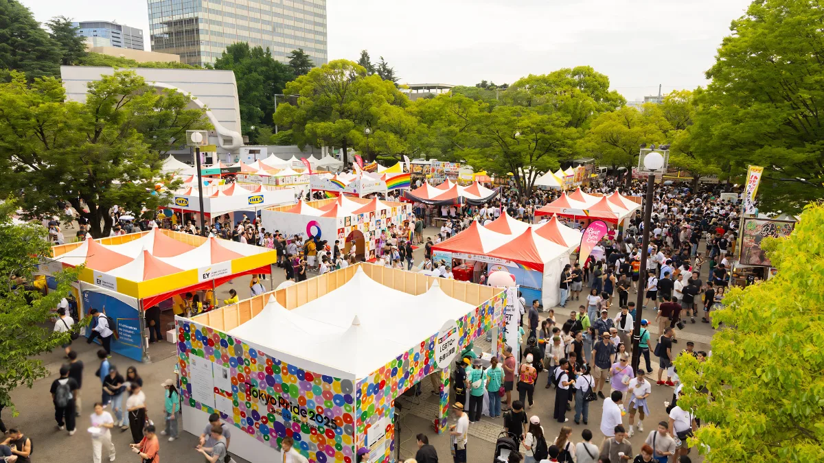 An elevated view of the Tokyo Rainbow Pride festival grounds at Yoyogi Park. The bustling outdoor event features crowds of people exploring corporate sponsor booths and community tents during the Tokyo Pride 2025 celebrations, highlighting the scale of Japan's largest LGBTQ+ pride festival.