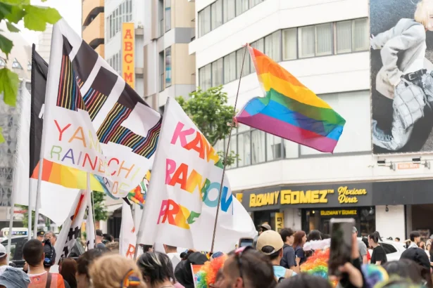 A vibrant scene from the Tokyo Pride Parade featuring a crowd waving rainbow flags and official community flags on the streets of Shibuya. This lively gathering showcases the celebratory atmosphere of the Tokyo Rainbow Pride festival.