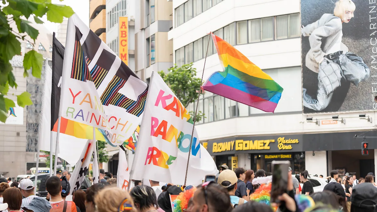 A vibrant scene from the Tokyo Pride Parade featuring a crowd waving rainbow flags and official community flags on the streets of Shibuya. This lively gathering showcases the celebratory atmosphere of the Tokyo Rainbow Pride festival.
