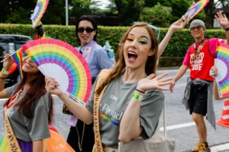 People celebrating at Tokyo Pride with rainbow fans, Pride flags and colourful makeup, supporting an lgbtq friendly Japan.