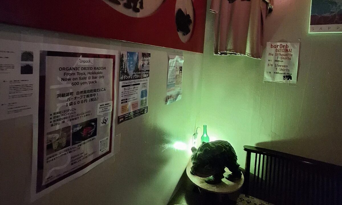 The interior of Bar Orb. Menus in English and Japanese adorn the walls. A small statue of a boar is backlit by green light.