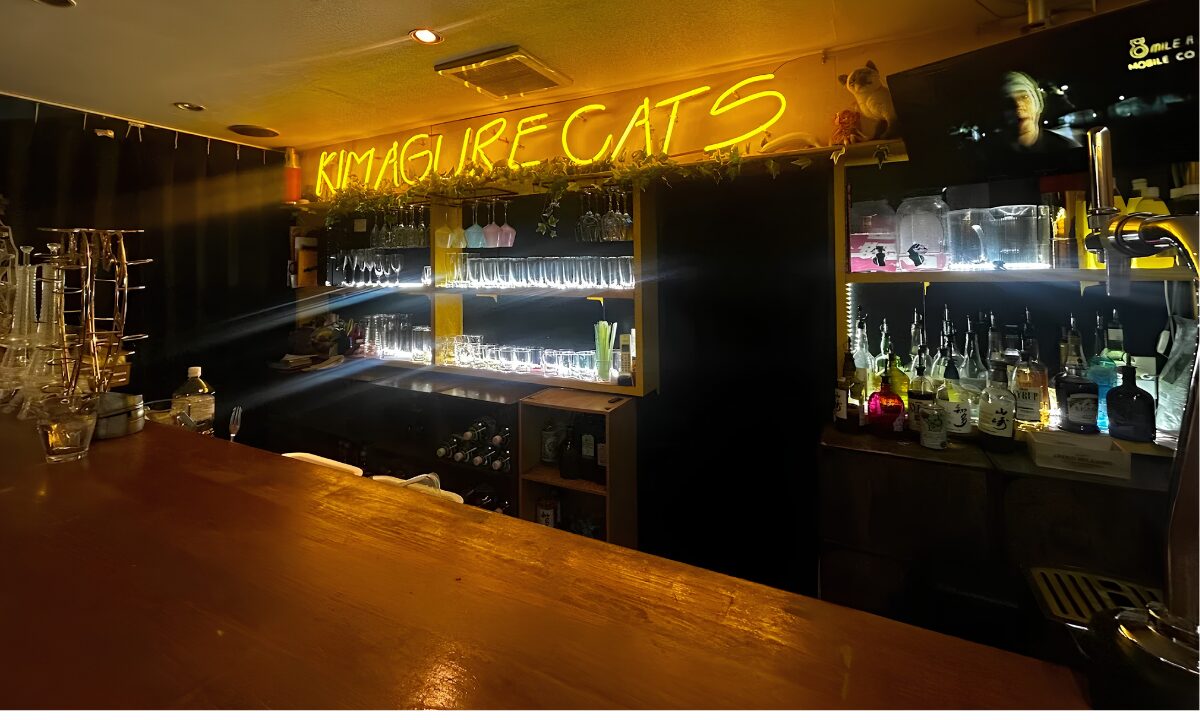 The interior of Kimagure Cat's. The name of the bar is written in neon lettering above a bar