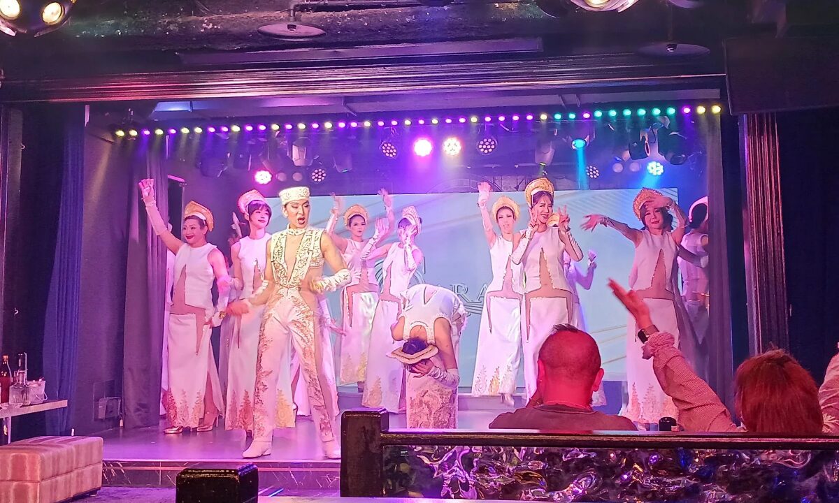 Performers at Gyasara on stage. Purple neon light bathes the stage as the women sing and dance in white outfits