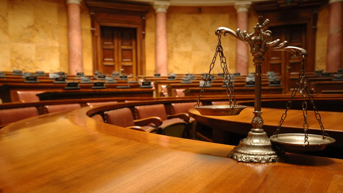 Osaka High Court Says Japan Should Recognize Non-Binary People in Family Registry 12 An ornate, empty courtroom with wooden seating and marble pillars, featuring a brass balance scale in the foreground on a polished wooden desk.