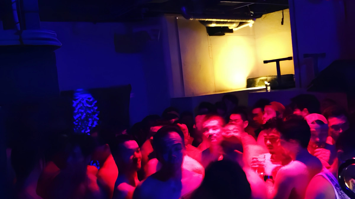 Image of inside of Boiler Room during event. Photo shows many people dancing in dark room, lit up with lights during party.