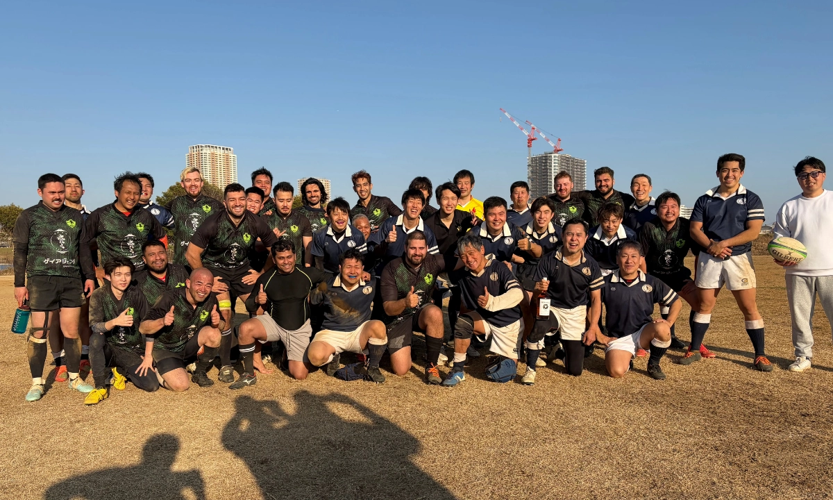 The Tsurumi Brats and another rugby team line up together, laughing, smiling, and some with thumbs up