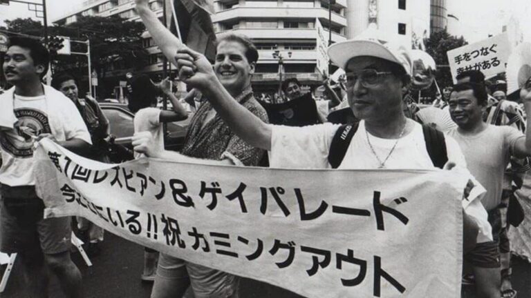 Teishiro Minami, on the right, leads the parade. He is holding the left side of a banner reading “The First Lesbian and Gay Parade” in Japanese