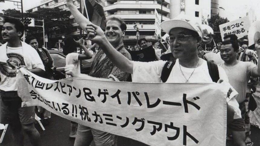 Teishiro Minami, on the right, leads the parade. He is holding the left side of a banner reading “The First Lesbian and Gay Parade” in Japanese