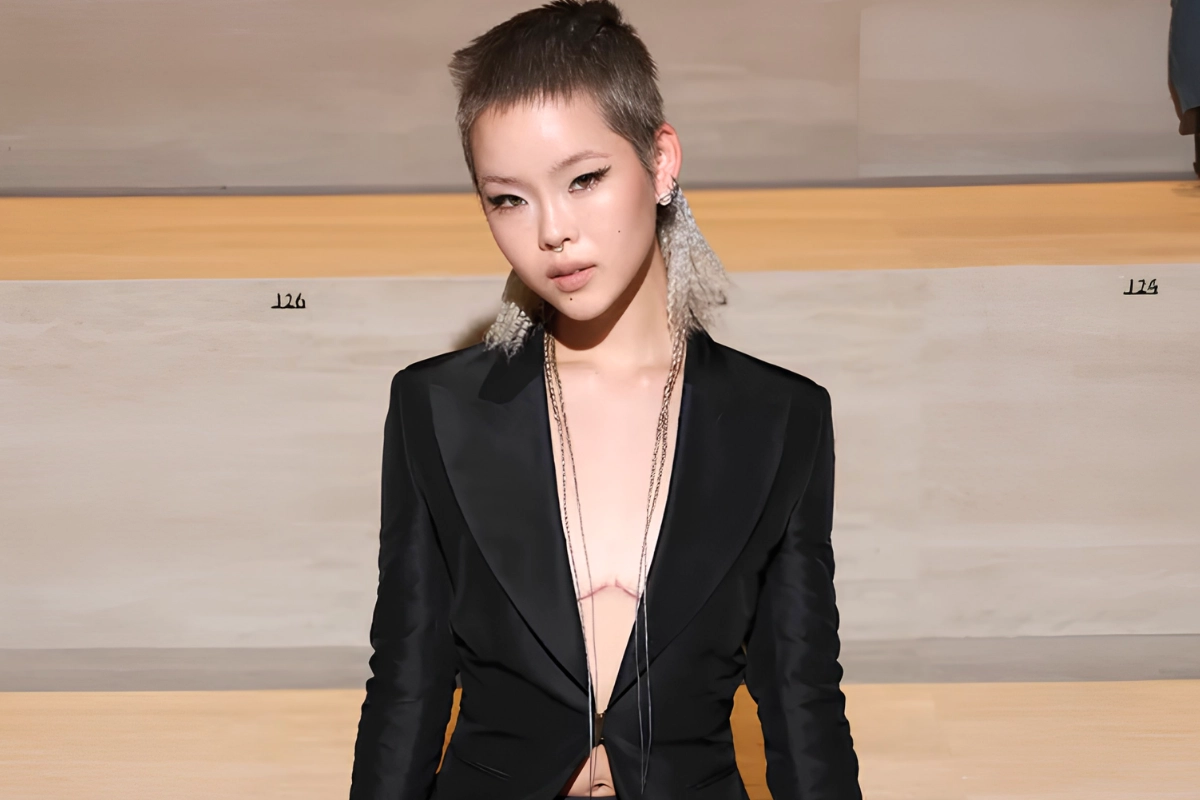 LGBTQ+ Japanese Celebrities to Know, From Pioneers to Today 32 Cocona wears a plunging black suit jacket and long necklaces as they sit and pose for photos at a fashion show