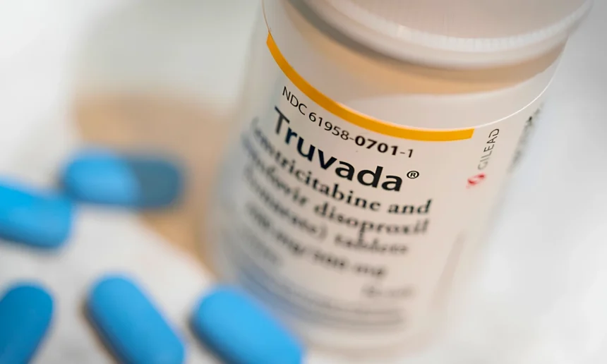 Close-up of a Truvada prescription bottle surrounded by several blue tablets on a white surface.
