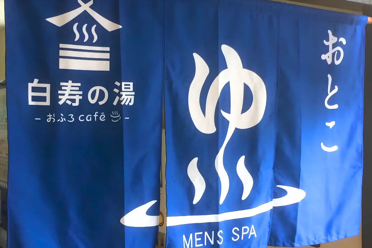 Blue noren curtains at a Japanese men’s spa entrance, featuring hot-spring symbols and Japanese text alongside the words “MEN’S SPA.”