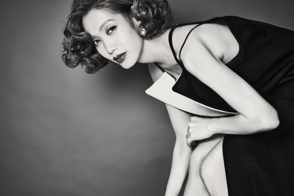 LGBTQ+ Japanese Celebrities to Know, From Pioneers to Today 23 Ataru Nakamura poses in a classic-style hairdo and black and white dress, while crouching over and staring into the camera. The photo is in black and white